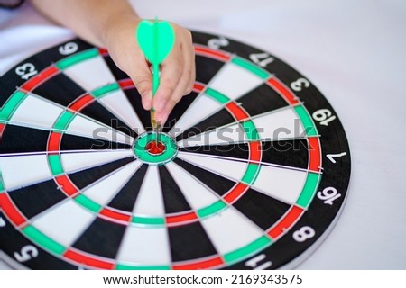 Hand with arrow throw hitting the center of bullseye target or dartboard.