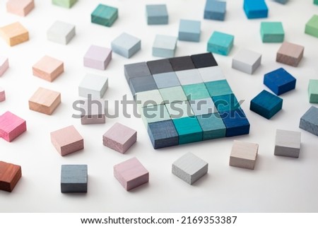Playing with colors. Color selection. Grey and light blue color sample cubes arranged on a natural white background, with pink, white, and blue grey cubes surrounding it. flat lay or top view.