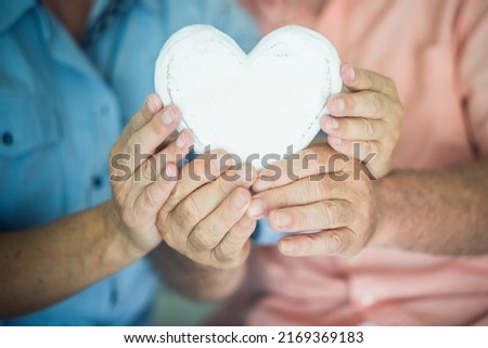 Close up of heart shape wooden decoration object. Concept of healhty senior lifestyle. Heart attack concept. Love and relationship with old mature man and woman hands. Together forever life. Dating