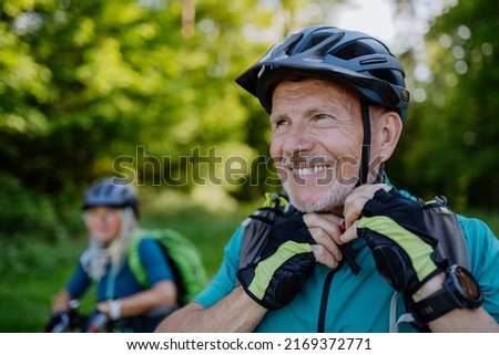 Active senior couple riding bicycles at summer park, man is putting on helmet, healthy lifestyle concept.