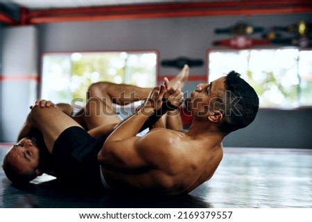 You must know your opponents weakness and abuse it. Shot of two male fighters wrestling on the floor at the gym.