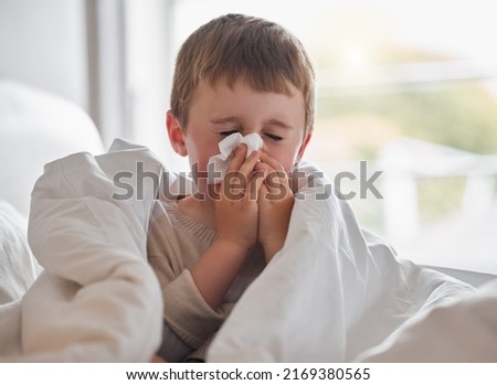 My nose wont stop dripping. Shot of a little boy feeling ill in bed at home and blowing his nose. Royalty-Free Stock Photo #2169380565