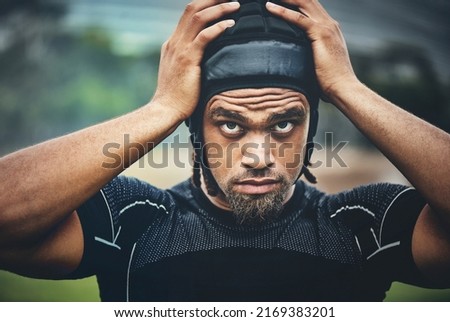 I'm ready to play some rugby. Cropped shot of a handsome young rugby player adjusting his headgear while standing on the field during the day. Royalty-Free Stock Photo #2169383201