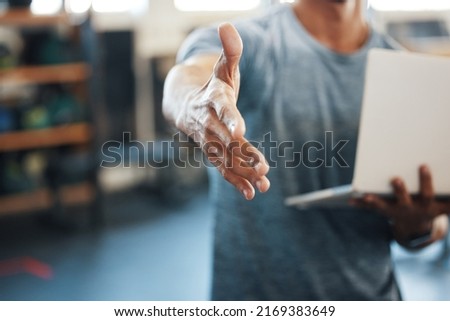 Congrats on signing up with us. Closeup shot of an unrecognisable man extending a handshake while using a laptop in a gym.