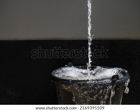 Black plastic bucket overflowing with water  Royalty-Free Stock Photo #2169395509