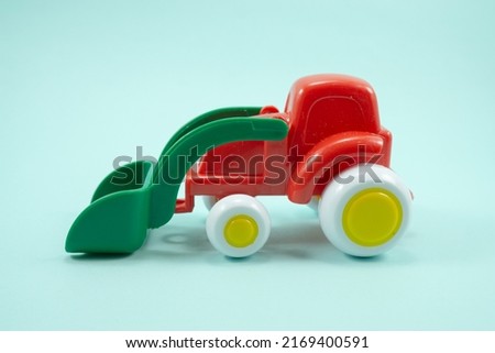 red paint plastic toy bulldozer with green universal blade isolated on blue background