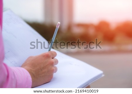 Student girl writing with pencil in open notebook sitting on street bench close view