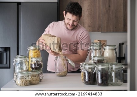 Young latin man filling up a jar with oat flakes from a paper bag. Food in bulk delivery. Royalty-Free Stock Photo #2169414833