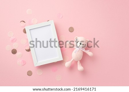 Baby girl concept. Top view photo of photo frame knitted teddy-bear toy and shiny confetti on isolated pastel pink background with empty space