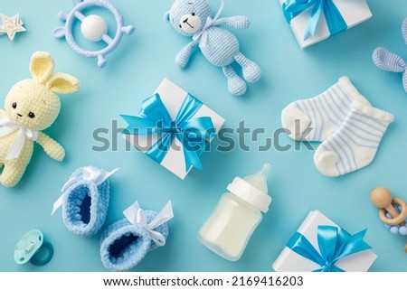 Baby accessories concept. Top view photo of gift boxes teether knitted bunny and teddy-bear toys socks booties soother milk bottle star and rattle on isolated pastel blue background