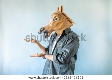 Funny horse head on human body on a green shirt on blue background, and showing to the left . Clip art, negative space. Royalty-Free Stock Photo #2169426129