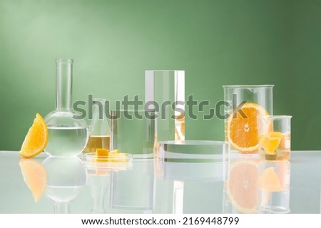 Front view of orange decorated with glassware and transparent podium in green background 