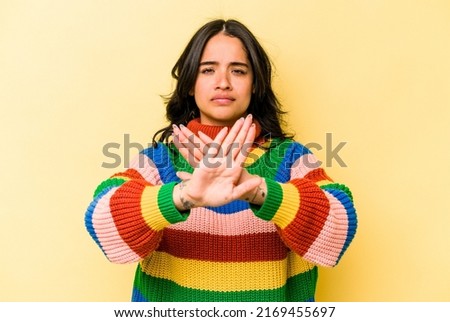 Young hispanic woman isolated on yellow background standing with outstretched hand showing stop sign, preventing you.