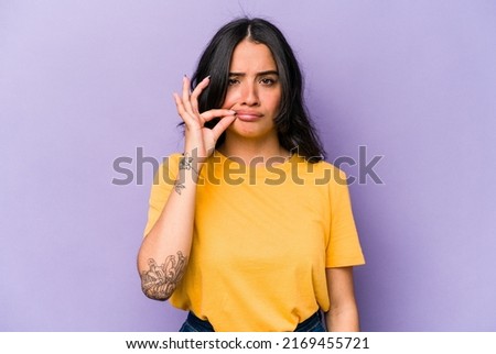 Young hispanic woman isolated on purple background with fingers on lips keeping a secret.