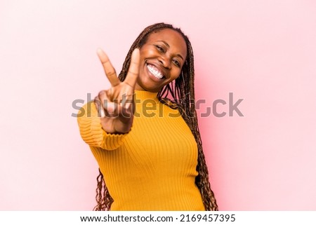 Young african american woman isolated on pink background joyful and carefree showing a peace symbol with fingers. Royalty-Free Stock Photo #2169457395