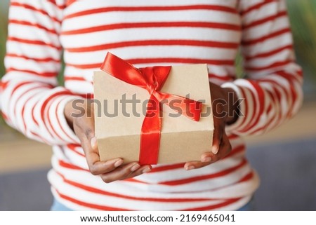 african American woman gives or receives a gift. a happy millennial woman with a cardboard box and a red ribbon in her hands. an anniversary and birthday gift for a friend or wife. party joy and