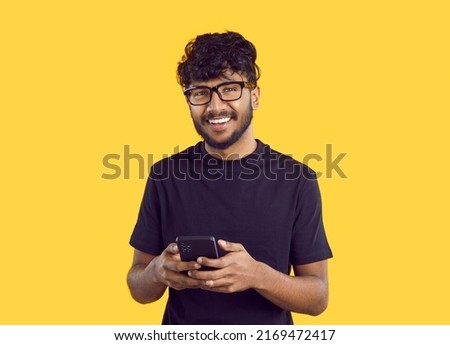 Crop shot of smiling millennial Indian guy in glasses isolated on yellow studio background using modern smartphone. Happy young biracial man text or message online on cellphone. Communication. Royalty-Free Stock Photo #2169472417