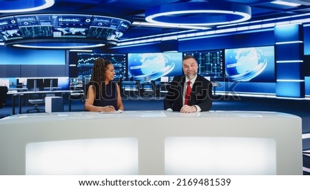 TV Live News Program: Two Professional Presenters Reporting On the Events. Television Cable Channel Newsroom Studio: Male and Female Anchors Talk. Mock-up Broadcasting Network Concept. Wide Shot Royalty-Free Stock Photo #2169481539