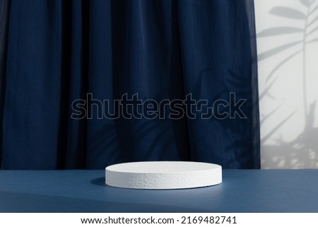 White cylindrical podium, pedestal on a blue background with curtain and palm shadow. Scene for the presentation of a cosmetic product. Empty showcase. Royalty-Free Stock Photo #2169482741