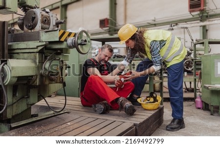 Woman is helping her colleague after accident in factory. First aid support on workplace concept. Royalty-Free Stock Photo #2169492799