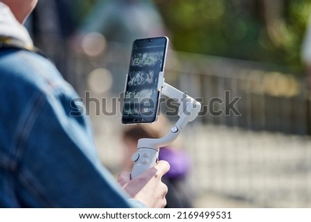 Blogger filming outdoor event on smartphone with gimbal stabilizer, video blogging for new followers. Video shooting content for social media networks, vlog video making Royalty-Free Stock Photo #2169499531