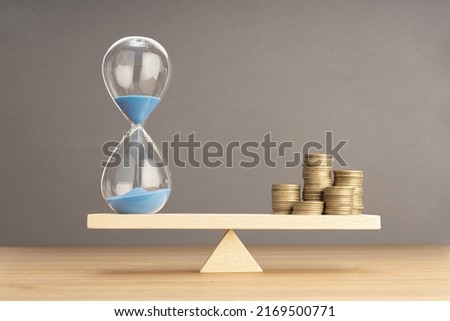 Balance Between Time and money concept. Sand clock and stacked coins on Seesaw. Copy space