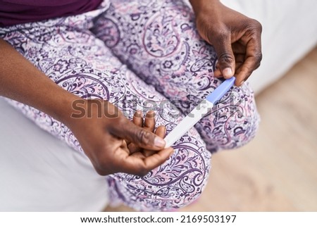 African american woman holding pregnancy test sitting on bed at bedroom