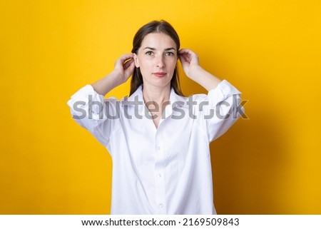 Young woman in a white shirt straightens her hair on a yellow background.