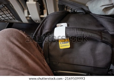 Cabin bag on a flight with tag for carry-on size guarantee fit between legs and under seat in front Royalty-Free Stock Photo #2169509993
