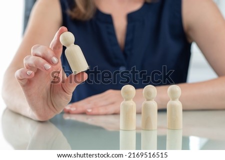 Recruiting employees. Wooden man in front of recruiter. Concept of personnel selection for company. Recruitment for business. Girl chooses one candidate from several. Recruiter interview metaphor Royalty-Free Stock Photo #2169516515