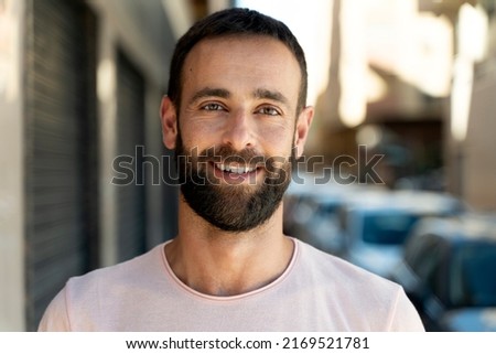 Closeup portrait of handsome smiling hispanic man looking at camera standing on urban street. Bearded hipster guy posing for picture 