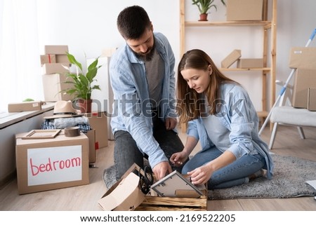 A man is cleaning in the living room after moving to a new apartment, unpacking cardboard boxes of things, the boy finds a picture in a frame from his childhood, he is shocked happy, watches with joy Royalty-Free Stock Photo #2169522205
