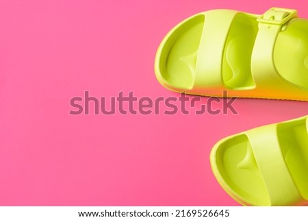 Top view of women's trendy pool sandals in green neon color isolated on the pink summer background. Summer vacation concept. Trendy colors for summer footwear. Sale time.