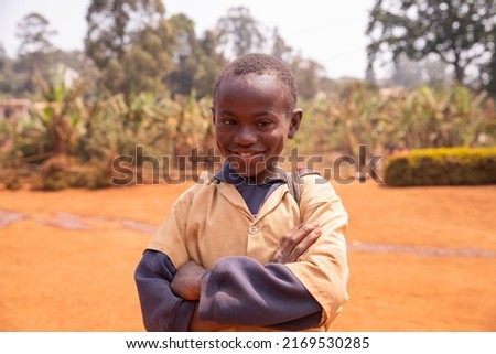 Smiling happy little african schoolchild with Down syndrome stands at schoolyard. Royalty-Free Stock Photo #2169530285