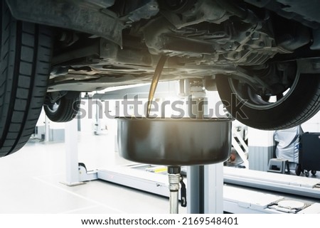 Engine oil change in car service. Auto is on hydraulic lift in garage workshop, process of draining old dark used oil Royalty-Free Stock Photo #2169548401