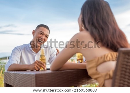 A young man and woman on a first date going very well. A couple laughing and having a great time while drinking beer at an outdoor cafe or bar during the late afternoon. Dating chemistry concept.