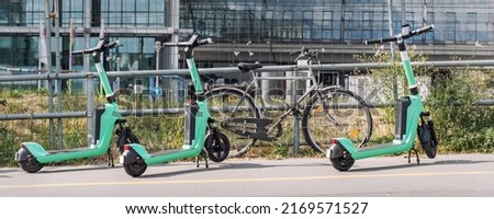 Many modern green electric scooters sharing parked city street. Self-service street transport rental service. Rent urban mobility vehicle with smartphone application. Zero emission green eco energy Royalty-Free Stock Photo #2169571527