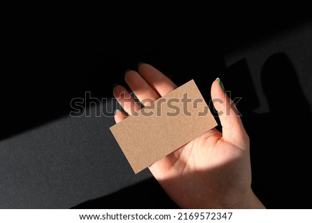 Female hand holding blank businesscard. Creative photo with shadow