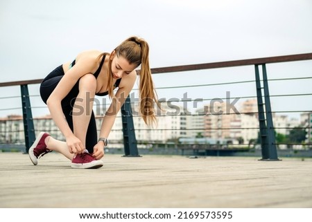 Young brunette woman wearing sportive clothes on city park, outdoors tying lace running shoes getting ready for run. Jogging girl exercise motivation health and fitness.