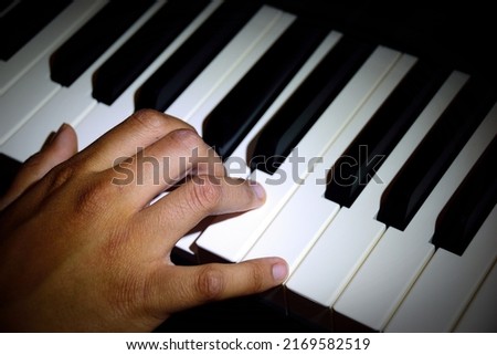 Close-up of a young performer's hand playing the piano with vignetting to focus attention on the main sibject.