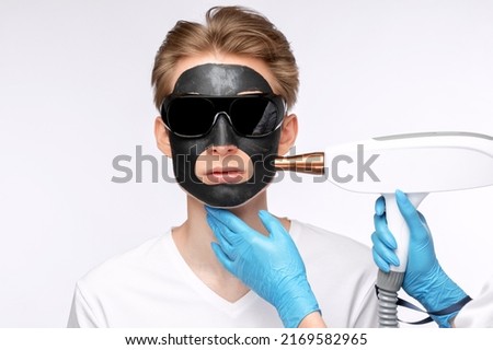 Beautician doing carbon peeling procedure to handsome guy in beauty salon. Hardware male cosmetology. Royalty-Free Stock Photo #2169582965