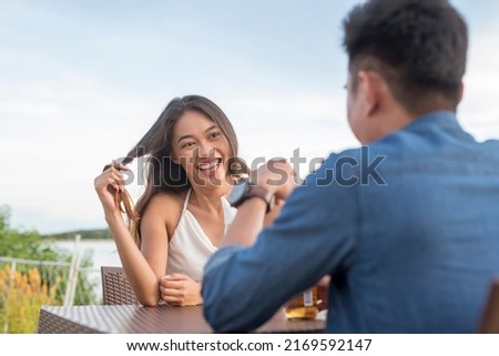 A young woman twirls her hair while listening intently to her date. Interested and attracted to a man she likes. A first date going well. Outdoor cafe scene. Royalty-Free Stock Photo #2169592147
