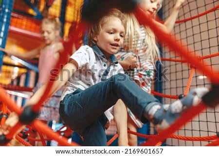 Excited kids playing together on net ropes. Happy group of siblings playing together on indoor playground. Cute school kids playing on the colorful playground at shopping mall Royalty-Free Stock Photo #2169601657