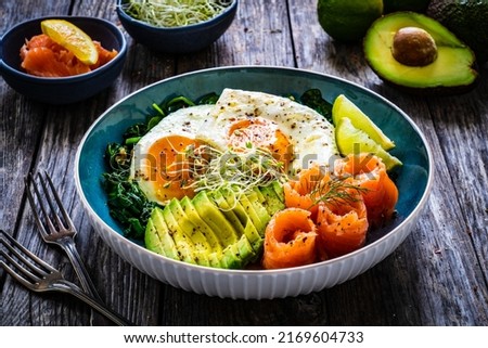 Salmon salad - smoked salmon, sunny side eggs, avocado and spinach on wooden table