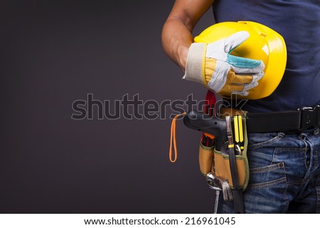 Close up of a worker with toolbelt and helmet against black background Royalty-Free Stock Photo #216961045