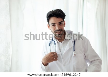 Portrait of a handsome, confident male doctor standing in the clinic. dressed in a doctor's uniform have headphones over the neck happy smile a doctor who specializes in treating patients