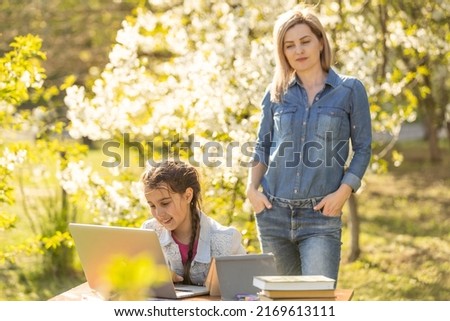 Mother helping her little daughter to use laptop computer. Child studying at home doing her homework or having online lesson. Homeschooling concept.