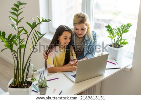 Happy mother with little kid daughter having fun online with application, watching video cartoons or playing game on laptop together, young babysitter or nanny teaching child girl to use computer