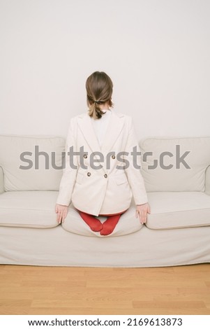 introvert behavior. a girl in red tights and a jacket stands back to front on the couch. psychological picture. Closed person. Stress and crisis. beige and red