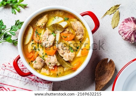 Chicken stew with potato and carrot in red pot, top view, copy space. Chicken soup with vegetables and herbs. Comfort food recipe. Royalty-Free Stock Photo #2169632215
